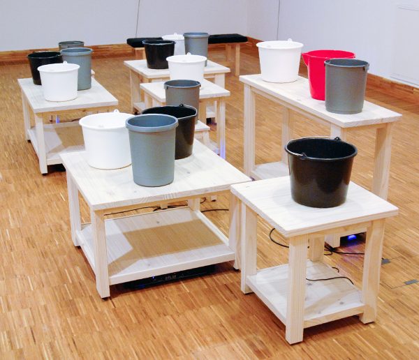 Gisela Motta - Chora Chuva - Installatie met 16 emmers gevult met water met 16 speakers op 6 tafels en 2 banken en 8 stereo versterkers