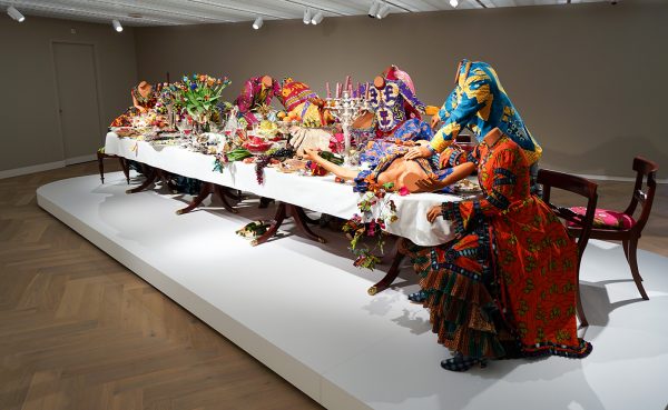 Yinka Shonibare - Last Supper - 13 glasvezel mannequins waarvan 1 met bokkepoten, batik kleding van Vlisco, tafels, stoelen, bestek, zilver, vazen, glaswerk, serviesgoed en glasvezel en hars voedsel