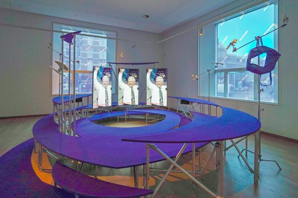 Hito Steyerl - Mission Accomplished, Belanciege - Driekanaals HD-video-installatie met omgevingssculptuur, kleur en geluid, 47,23minuten, 2019