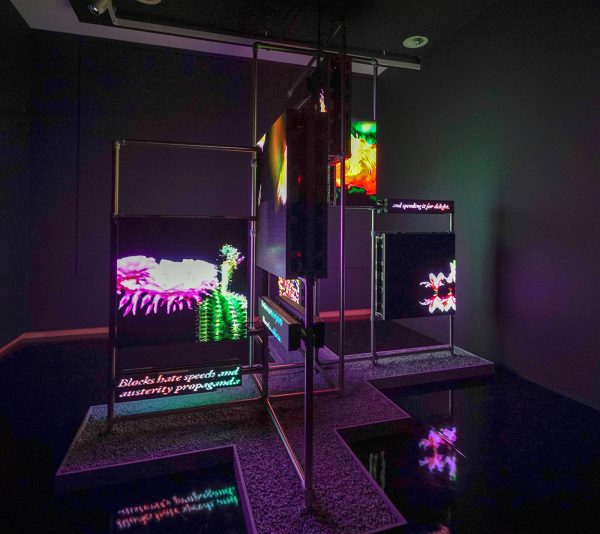 Hito Steyerl - Power Plants - Roestvrijstalen steigerconstructies, LED-panelen, scrollende LED tekstpanelen, gecementeerde MDF dozen, Olivijn grind, vinyl, meerkanaals videoloop, kleur en zonder geluid