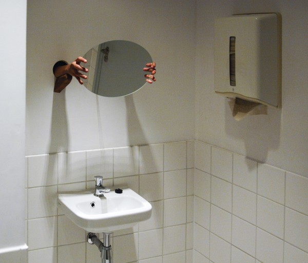 Laura Lima - Toilet - Toiletruimte en een persoon die de spiegel vast heeft