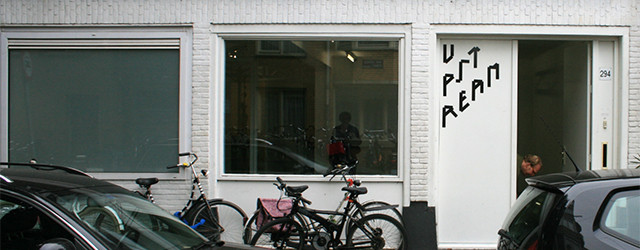 Flinke stukken klei hangen aan vlastouw aan een houten installatie. Iets verder in de galerie liggen vergelijkbare ladingen klei op een tafel. Het is rauw en doet denken aan hompen [&hellip;]